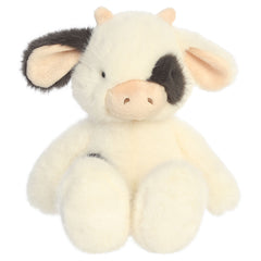 A cow plush toy from Aurora with eggshell fur, dark spotted accents, pink ears, and a softly weighted body.