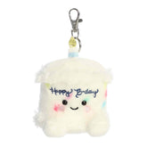 Plush keychain of a white birthday cake slice by Palm Pals with sprinkles, a blue candle, and rosy cheeks.