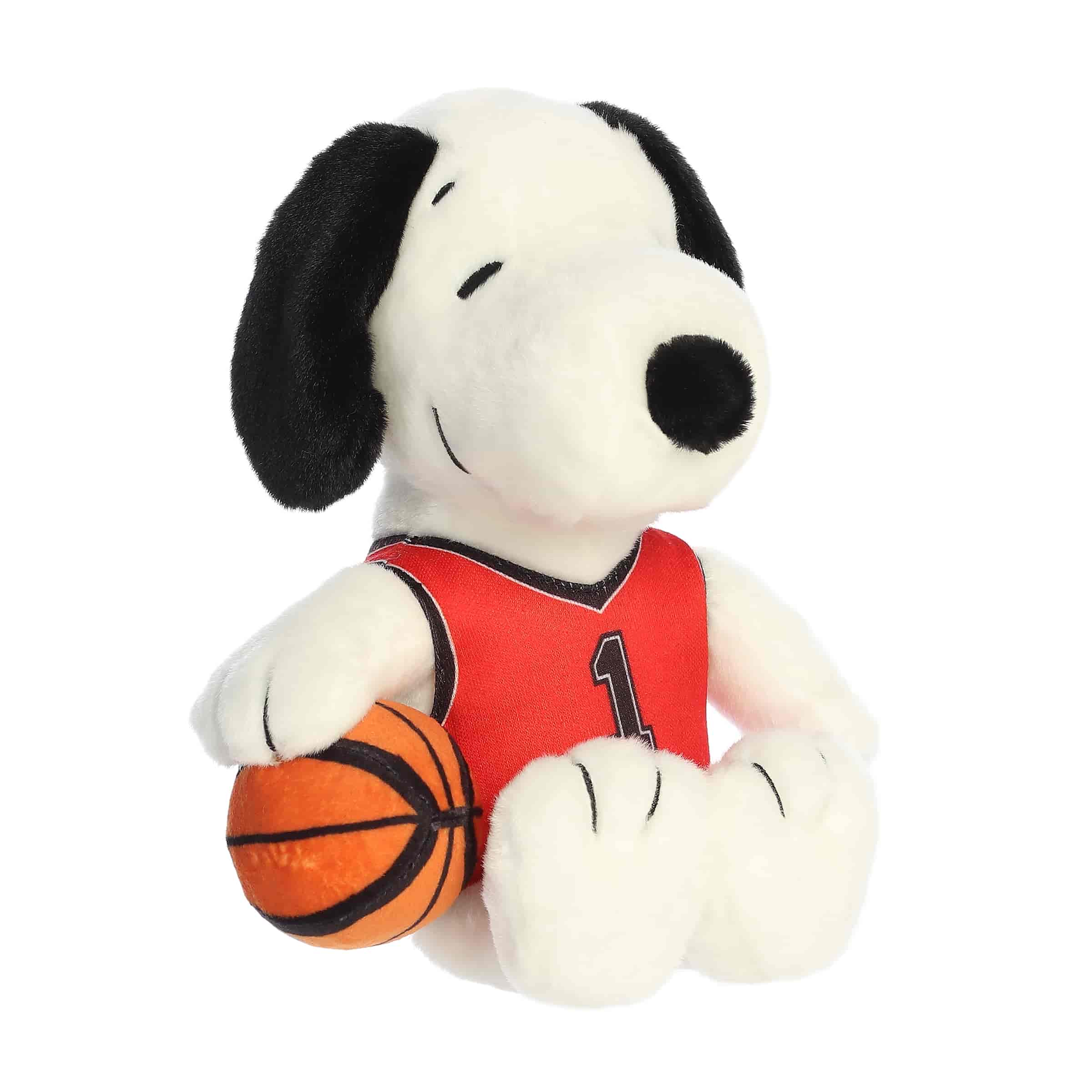 A Snoopy plush wearing a red basketball jersey and holding a basketball from the Peanuts collection
