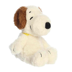 A Snoopy plush with soft white fur and brown ears lying down from the Peanuts collection by Aurora.
