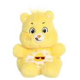Funshine Bear Palm Pals plush with soft yellow fur, cheerful smile, round ears, and smiling sun belly badge