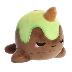 A green and brown Tasty Peach Nomwhal plush that is an expressive narwhal with the color scheme of an avocado