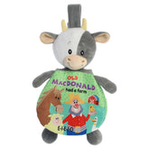 A black and white cow plush from ebba by Aurora with a soft body and attached Old MacDonald crinkle storybook.