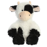 A black and white plush toy from Aurora with spotted fur, small horns, and an embroidered cow face.