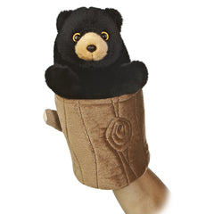 A black bear hand puppet toy from Aurora with black fur emerging from a brown tree stump.