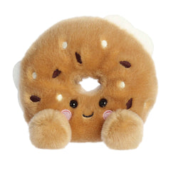 Plush toy of an everything bagel in the Palm Pals collection with seed toppings and a smiling face.