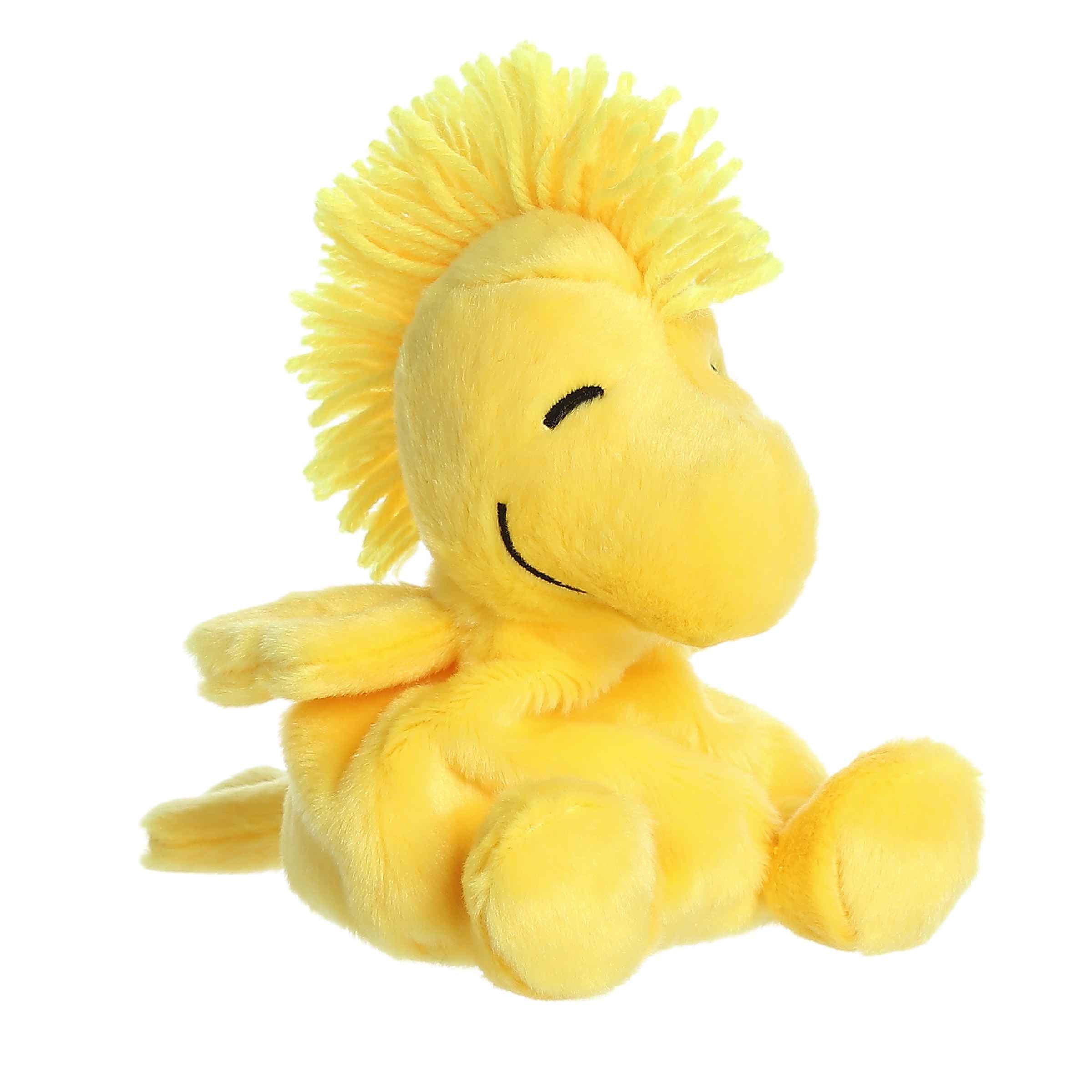Bright yellow Woodstock Palm Pals plush from the Peanuts collection with tuft of hair, embodies friendship, is a tiny bird