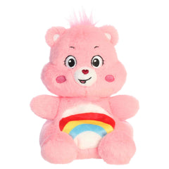 Cheer Bear Palm Pals plush with soft pink fur, sweet smile, round ears, and colorful rainbow belly badge