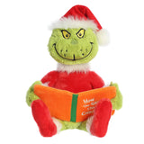 Green Grinch plush doll wearing Red Santa outfit, sitting and holding 'How the Grinch Stole Christmas' book