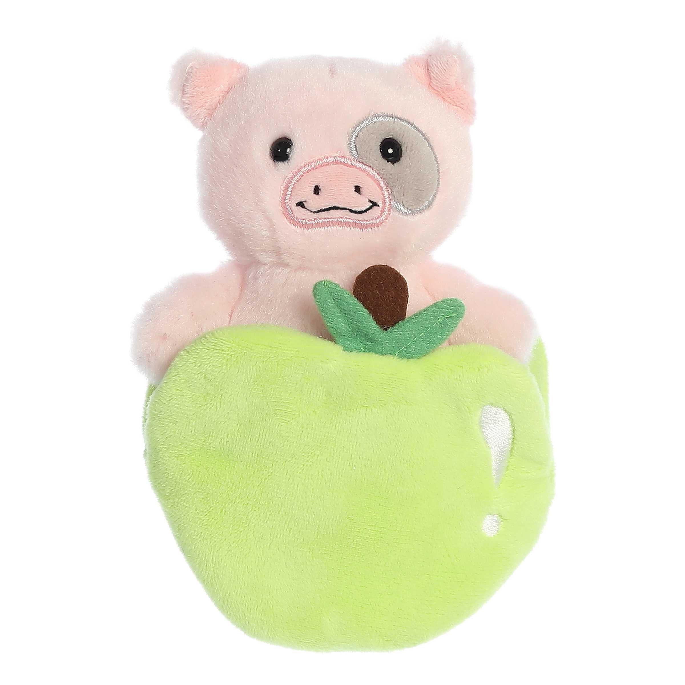 Cute pink Piglet plush rattle toy with smiling face and gray accent on eye sitting inside a crinkly green apple pocket