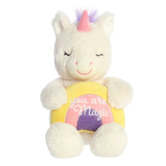 White plush unicorn seated, holding a rainbow with 'You Are Magic', contrasting with a pink horn and purple mane
