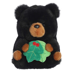 Adorable black bear with brown accents on their mouth and stubby hands and feet holding holiday holly leaves