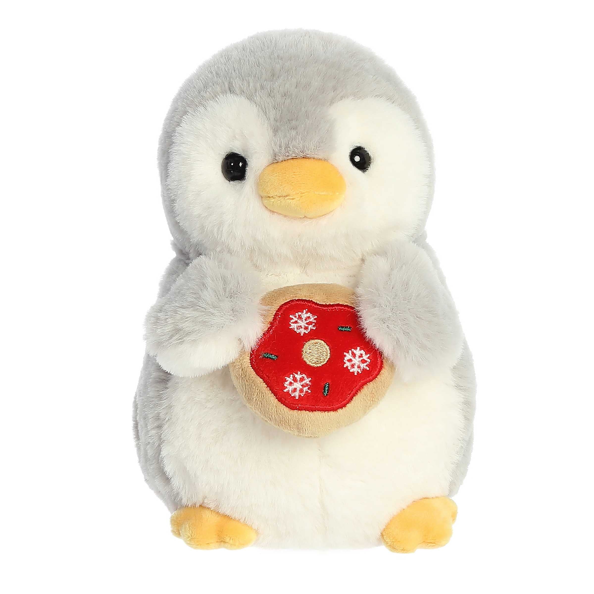 Adorable light grey penguin with yellow beak and feet holiding a donut with red frosting, green sprinkles, and snowflakes